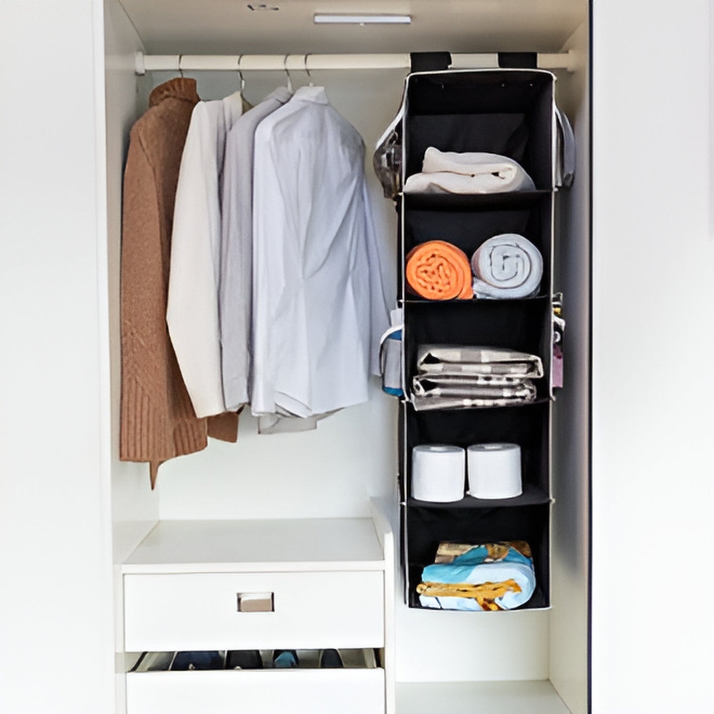 Closet with hanging clothes and a black vertical organizer.